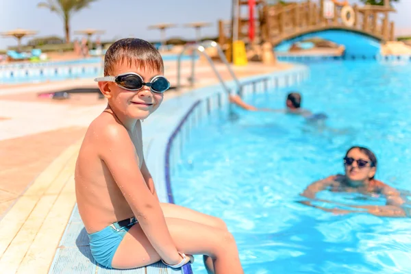 Lächelnder glücklicher Junge, der am Rande eines Pools sitzt — Stockfoto