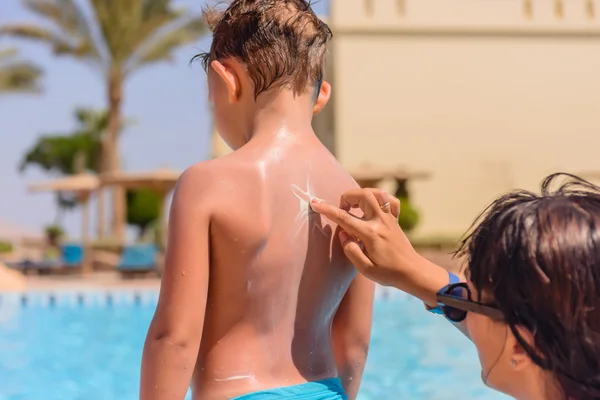 Giovane madre sfregamento crema solare su suo figlio — Foto Stock