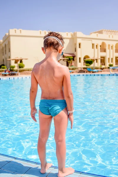 Young boy standing on the edge of a resort pool — Stock Photo, Image