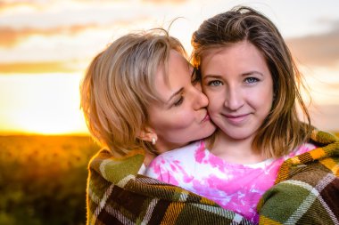 Mother kissing her young daughter at sunset