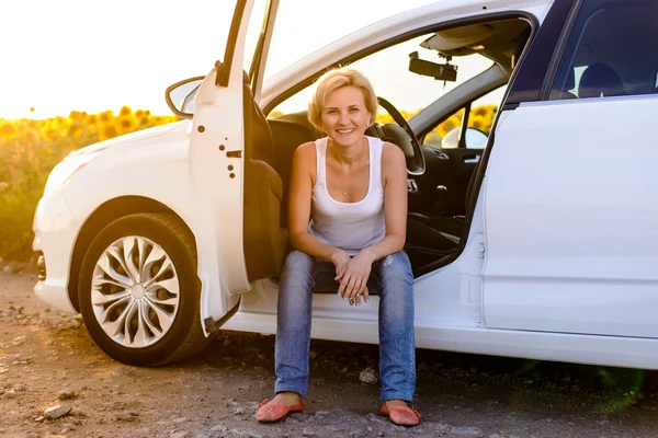 Smiling woman sitting in the open door of her car — Stockfoto