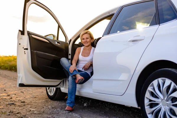 Smiling woman sitting in the open door of her car — Stok fotoğraf