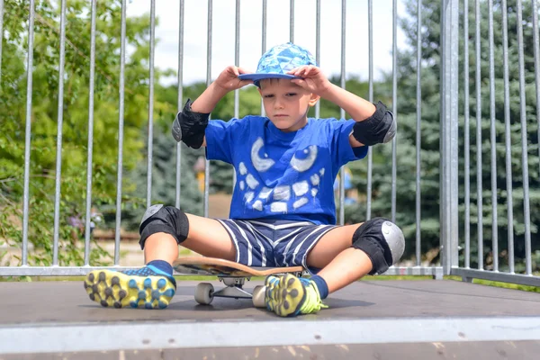 Cheeky young boy sitting on his skateboard — Stock Photo, Image