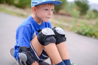 Bir kaykay üzerinde oturan düşünceli küçük çocuk
