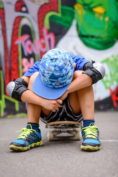 Giovane ragazzo seduto a riposo sul suo skateboard — Foto Stock