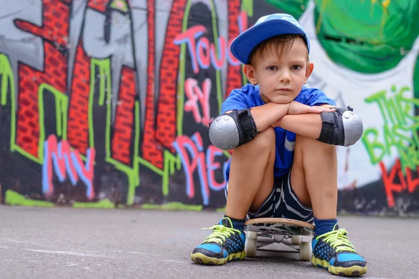 Attraktiver kleiner Junge sitzt auf seinem Skateboard — Stockfoto