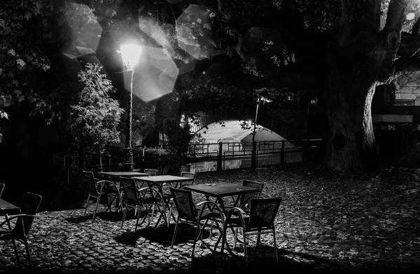 Night life , lonely empty restaurant tables under the city lights in the trees on the background of the illuminated bridge