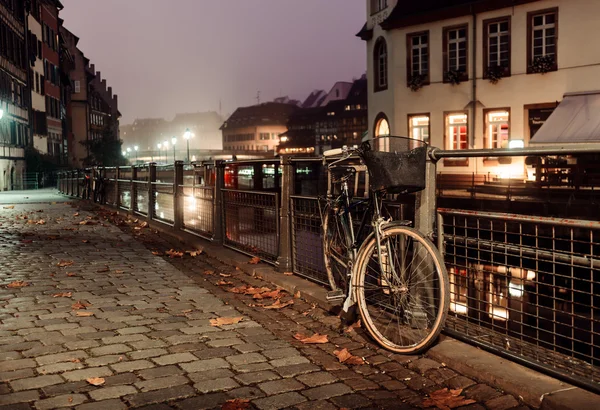 Oude fiets op stad keien vastgemaakt aan het hek verlicht door de lichten van de nacht-stad — Stockfoto