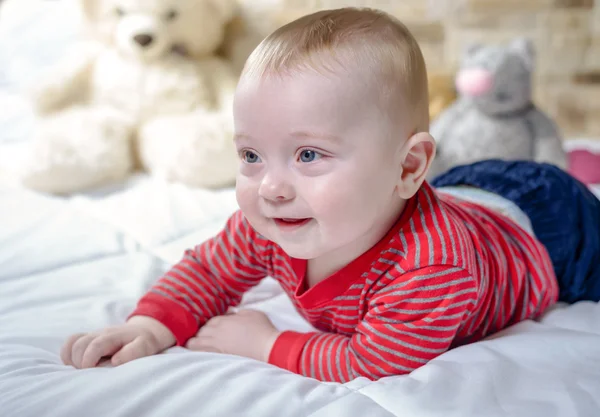 Closeup portrait view of one funny smiling cute little baby boy with blonde hair lying on bed with soft blanket looking forward — Stock Photo, Image