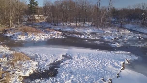 Volare all'indietro a mezz'aria con un drone sul fiume ghiacciato con alcune rapide e neve — Video Stock