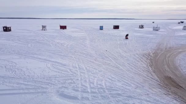 Kışın gün batımında bir kar aracının çocuklarla gezintiye çıktığı bir buz balıkçısı köyünün hava görüntüleri. — Stok video