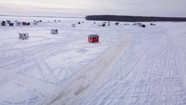 Volando lejos de la aldea de chozas de pesca de hielo con un dron sobre el lago congelado con un cielo parcialmente nublado — Vídeo de stock