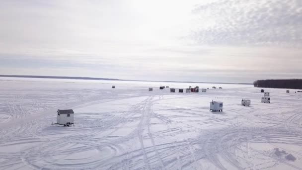 Retour en avion avec un drone, s'éloignant du village de pêcheurs sur glace avec un beau coucher de soleil en arrière-plan — Video