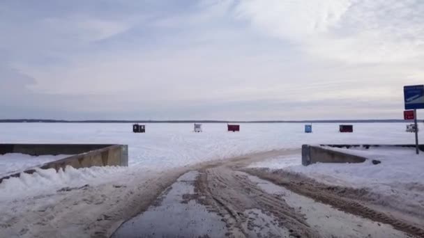 Lecąc nad rampą mariny i do zamarzniętego jeziora pokazując kilka lodowych chatek rybackich i piękny zachód słońca — Wideo stockowe