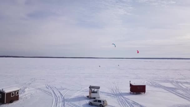 Buz balıkçı kulübelerinin üzerinden uçmak, kışın donmuş göldeki uçurtma sörfçüsüne yaklaşmak. — Stok video