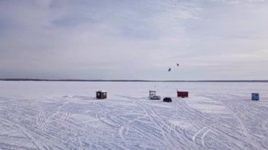 Donmuş gölün üzerinde uçan kısa bir video kardaki izleri, buzda balık avlama kulübelerini ve arka plandaki uçurtma sörfçülerini gösteriyor.