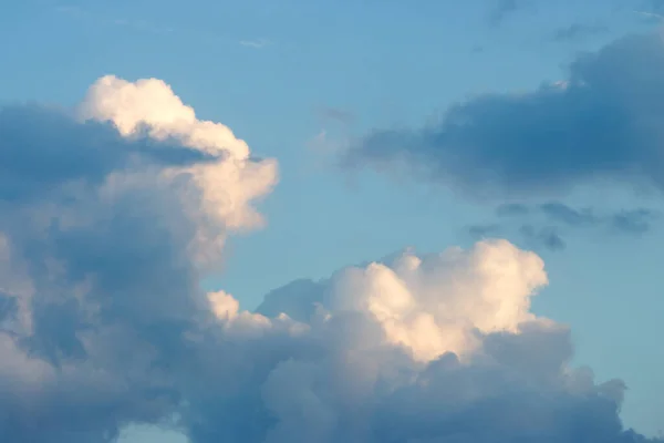 Mavi gökyüzünde büyük beyaz bulutlar ve ön planda fırtınalı bulutlar.