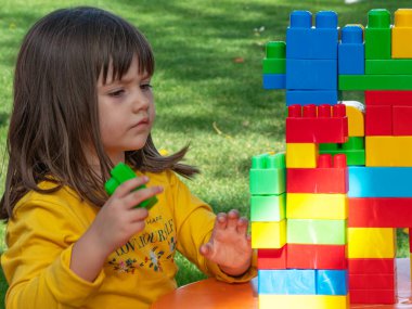 Güneşli bir sonbahar sabahı bahçesinde inşaat oyunu olan bir kule inşa eden bir kız.