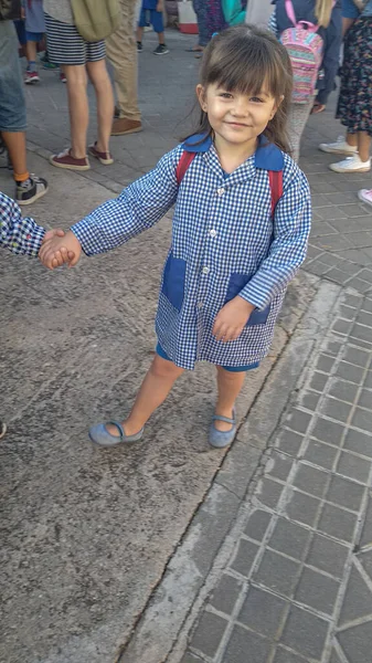 Girl with a smock at school door, holding hands with a friend just before entering class