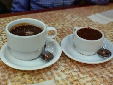 Küçük bir fincan çikolatanın yanında büyük bir fincan sıcak çikolata.