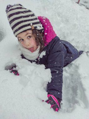 Küçük kız karda oynuyor ve surat yapıyor.