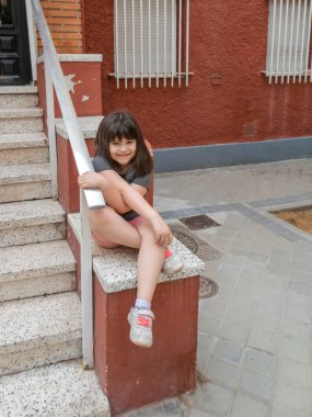 Gülümseyen küçük kız bir yaz günü kapı eşiğindeki merdivenin yanında oturuyor.