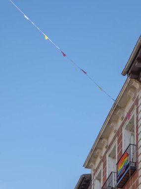Güneşli bir yaz gününde sokaklarda Gay Gururu bayrağıyla balkonların arasına asılmış pankartlar.