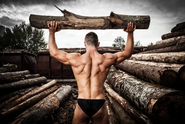 Hombre musculoso fuerte con troncos de madera — Foto de Stock