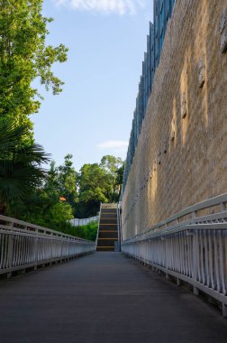 Uzağa uzanan metal çitleri olan ve merdivenlerde dinlenen bir kaldırım. Sarı katıksız duvar. Dar palmiye ağaçları ve yeşil ağaçlar. Dikey