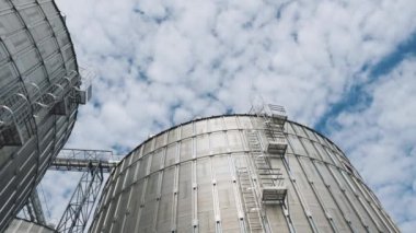 Büyük tahıl asansörlerinin tepesinde. Hareket eden gökyüzünün altında gümüş tarım konteynerleri. Güneşli bir günde depolama için metal tanklar.