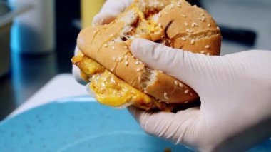 Lezzetli fast food. Şef taze burgeri ikiye ayırıyor. Et pirzolası, erimiş peynir, sebze ve soslu büyük iştah açıcı çizburger..