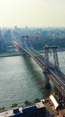 Williamsburg Köprüsü 'nün çelik yapısı, trafik ve yoğun şehir arkaplanı. Doğu Nehri 'nin sularının havadan görünüşü. Dikey video.