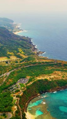 Hawaii, Oahu 'daki Hanauma hangarının havadan görüntüsü. Mercan kayalıkları, kumlu plajlar ve dolambaçlı bir yol ziyaretçileri bu tropikal bölgeye çeker. Dikey video.
