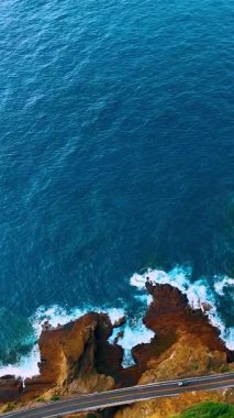 Hawaii, Oahu 'daki engebeli bir kıyı şeridinin havadan görünüşü. Aşağıdaki dalgaların ve araçların görülebildiği uçurumlara paralel giden bir yol var. Dikey video.