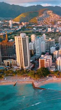 Honolulu, Oahu 'nun havadan görünüşü. Kumsal, iskele, turkuaz su ve bereketli dağlar canlı bir sahil kenti oluşturur. Dikey video.