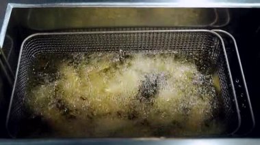 Sıcak yağa batırılmış patates dilimli metal kızartma sepeti. Yağ kızartma işlemi sırasında aktif olarak fokurduyor.