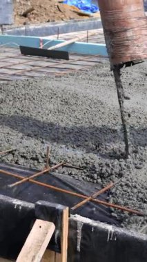 Hortumdan güçlendirilmiş çelik şebekeye taze beton dökülüyor. Temel çalışmaları devam ediyor. İnşaat alanı. Dikey video.