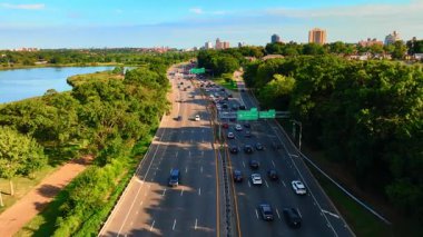 New York, Queens 'teki çok şeritli trafiği olan 678 numaralı eyaletler arası hava görüntüsü. Güneşli bir günde, gölün kıyısındaki yeşil ağaçların arasındaki yol..
