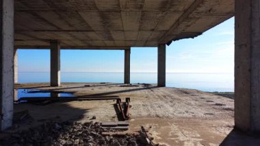 Beton sütunlar ve tavanda su birikintileri ve molozlar, sakin deniz manzaralı. Hava görünümü.
