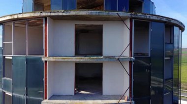 İnşaat halindeki yuvarlak binanın, eksik panelleri ve açıkta kalmış iç kısımları var. Kırsal zemin. Cam ve tuğla cepheli silindirik bir bina..