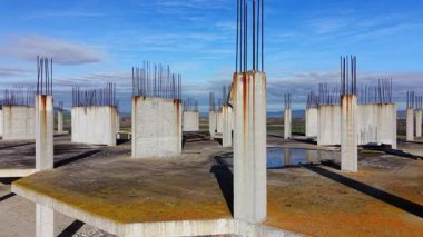 Tamamlanmamış çatı, dikey beton sütunlar, paslı demirler ve su birikintileriyle korunmasız çelik parmaklıklar. Hava ve su hasarı belirtileri var. Hava görünümü.