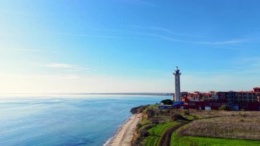 Sahil uçurumundaki kırmızı çatılı binaların yanındaki deniz feneri sakin suya ve berrak gökyüzüne bakıyor. Deniz kıyısındaki bir kasabanın havadan görünüşü.
