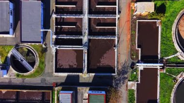 Üzerinde işlenmemiş su bulunan dikdörtgen ve dairesel tankların bulunduğu tesis, yürüyüş yolları ve borularla birbirine bağlı. Koyu sıvı ile karıştırılmış tank düzeni. Hava görünümü.