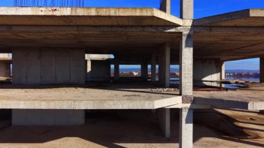 Terk edilmiş bir inşaat alanından geniş açıyla beton levhalar ve destek sütunlarını gösteriyor. Deniz ve kasaba açık duvarların arasından görülebiliyor..