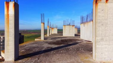 Çatıdaki beton demirle birden fazla beton sütunun perspektif görüntüsü. Mavi gökyüzünün altında yeşil tarlalar ve tepeler var. Hava görünümü.