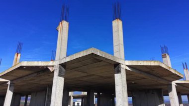Çelik demiri olan birkaç beton sütunun bir inşaat sahasındaki açık mavi gökyüzüne uzanan alçak açılı görüntüsü. Hava görünümü.
