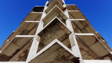 Açık mavi gökyüzüne karşı çok katmanlı güçlendirilmiş beton yapının keskin bir mimari köşesinin alçak açılı görüntüsü. Hava görünümü.