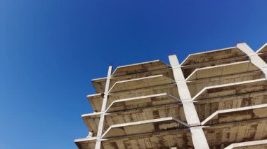 Düşük açılı bir yan görüş, açık mavi gökyüzüne karşı inşaat halindeki beton iskeletin birden fazla seviyesini gösteriyor. Havadan.