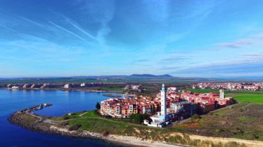 Mavi deniz kıyısındaki bir yarımadada, deniz feneri bulunan modern renkli bir sahil kasabasının yüksek açılı manzarası. Hava görüntüsü. Bulgaristan.