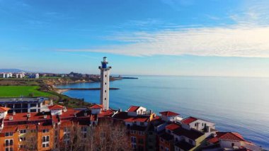 Mavi tavanlı, yüksek beyaz bir deniz fenerinin havadan görünüşü, kırmızı çatılı konut binaları, yeşil alanlar, ve berrak bir gökyüzünün altında sakin mavi bir deniz. Bulgaristan.